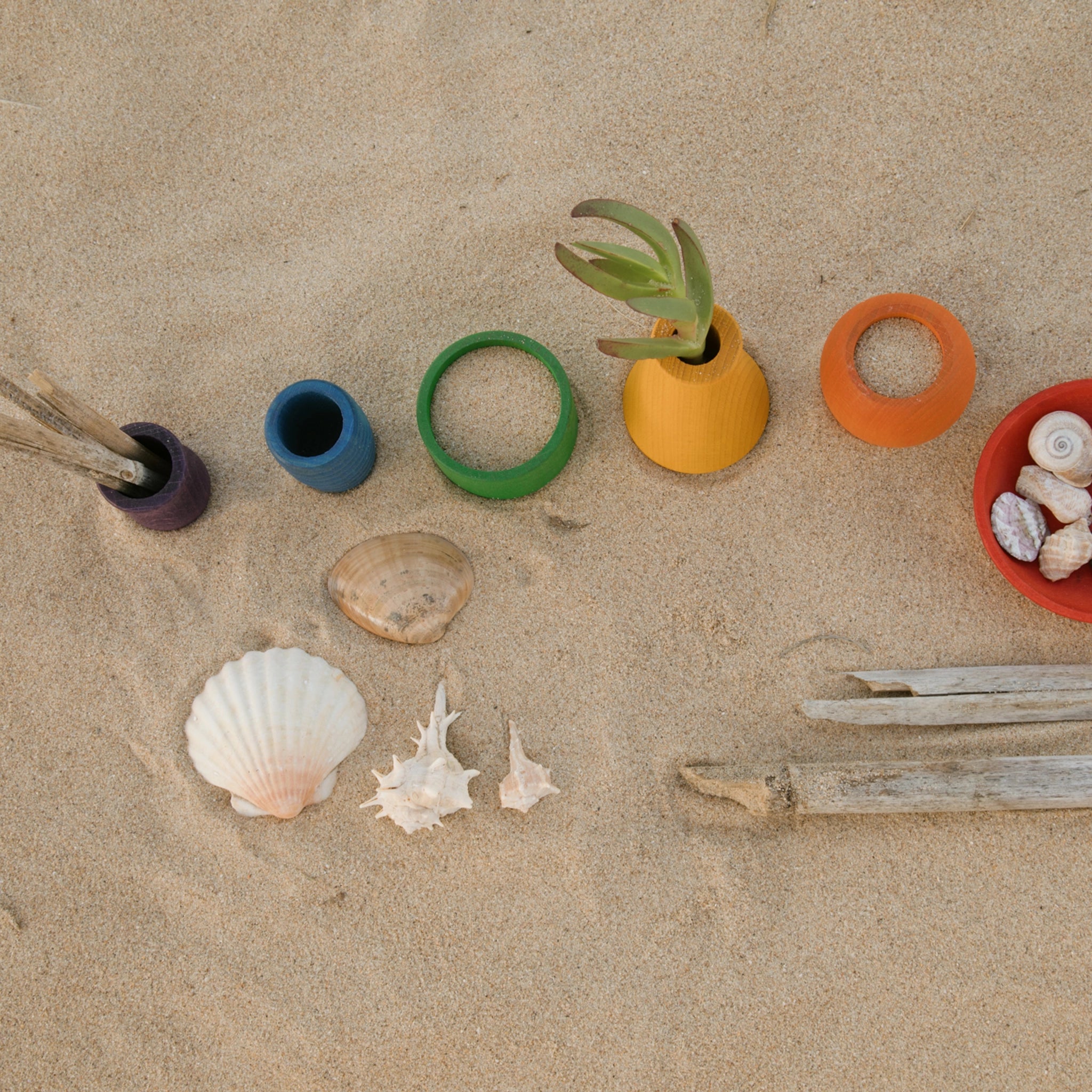 Freies Spiel: Pots, ein Set aus sechs handgefertigten, bunten Holztöpfchen auf Sand arrangiert, ideal für kreatives Spiel drinnen und draußen. Nachhaltig produziert in Spanien.