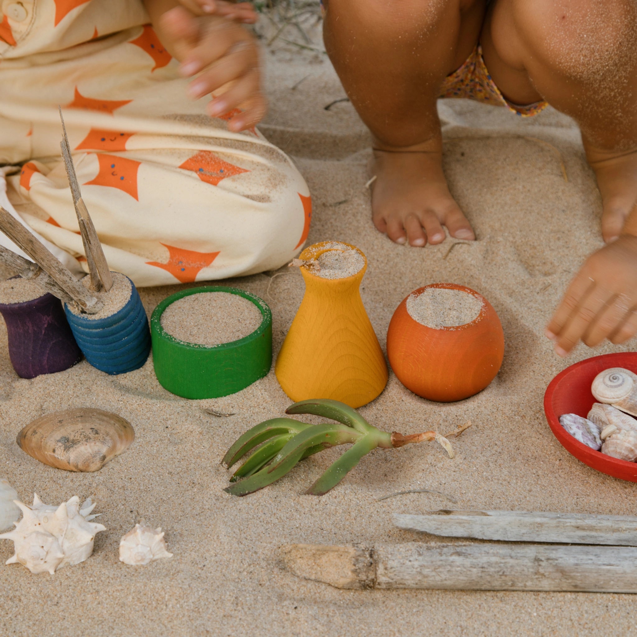 Freies Spiel: Pots aus nachhaltig geforstetem Holz. Ein Kind spielt im Sand mit den handgefertigten, bunten Töpfchen, ideal für kreatives Spiel drinnen und draußen. Perfekt für moderne, umweltbewusste Familien.