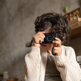 Ein Kind mit lockigem Haar hält eine Kamera und verkörpert den Entdeckergeist von Freies Spiel: Hello Winter! – ein Set aus fünf handbemalten Holzelementen, inspiriert von nachhaltiger Ästhetik.