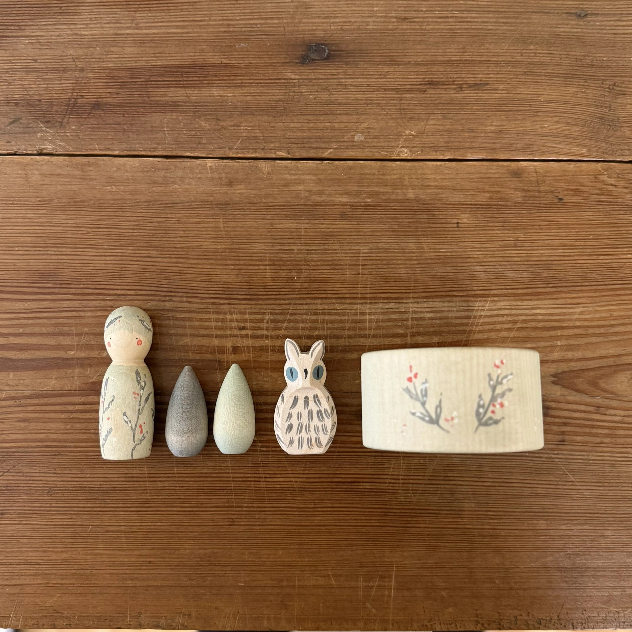 Freies Spiel: Hello winter! zeigt fünf handgefertigte Holzelemente auf einem Tisch: ein bemalter Peg-Doll, zwei tropfenförmige Blöcke, eine Eulenfigur und Washi-Tape, die winterliche Entdeckungen inspirieren.