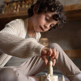 Ein Kind spielt mit Freies Spiel: Hello Winter!, einem Set aus nachhaltigem Holz mit handbemalten Elementen und einem stapelbaren Schloss-Spielzeug, das den Winter erkundet. Hergestellt von Grapat und Ostheimer.