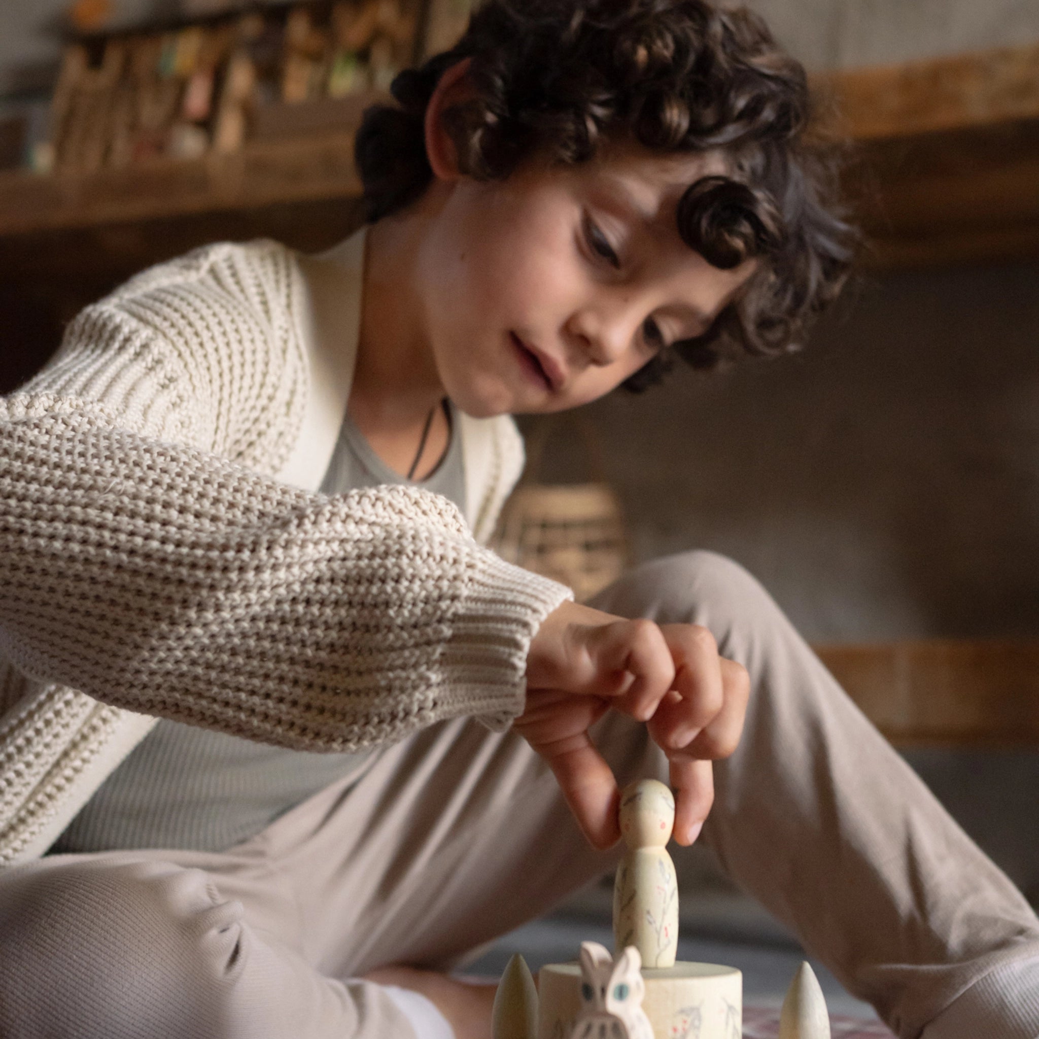 Ein Kind spielt mit Freies Spiel: Hello Winter!, einem Set aus nachhaltigem Holz mit handbemalten Elementen und einem stapelbaren Schloss-Spielzeug, das den Winter erkundet. Hergestellt von Grapat und Ostheimer.