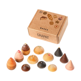 Freies Spiel: Bakes von Grapat zeigt ein Kinder-Backset mit einer braunen Schachtel und kleinen Holzgebäcken, die Kuchen und Kekse darstellen. Perfekt für kreatives Rollenspiel und nachhaltiges Design von KLICKKLACK.