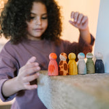 Ein Kind mit lockigem Haar spielt mit der Freies Spiel: Animal Crew von KLICKKLACK, handbemalte Holzfiguren in verschiedenen Designs, die liebevoll auf einer Teppichstufe arrangiert werden.