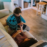 Zwei Kinder spielen auf einem Sofa mit dem Freies Spiel: Animal Crew Set. Eines hält bemalte Holzfiguren, das andere sitzt mit blauen Flügeln. Im Hintergrund Bücherregal und Holzstuhl.