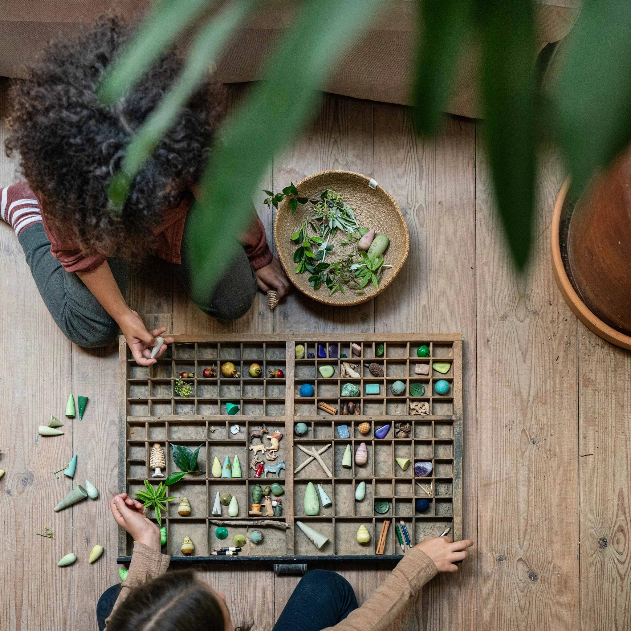 Zwei Kinder sortieren Naturmaterialien und Spielzeugfiguren, darunter das Produkt Freies Spiel: Animal Crew, in einem großen Holzkasten. Diese Aktivität spiegelt KLICKKLACKs nachhaltigen, ästhetischen Ansatz wider.