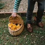 Eine Hand hebt den Deckel eines kleinen Korbkörbchens, das mit leuchtend gelben Pfifferlingen gefüllt ist, passend zum Produkt Freies Spiel: Forest Tree, das nachhaltige, regionale Ästhetik verkörpert.