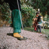 Ein Kind steht auf einer Schaukel, während im Hintergrund zwei Kinder neben einem Tisch mit Körben stehen. Freies Spiel: Forest Tree bringt natürlichen Spielspaß in den Garten, inspiriert von KLICKKLACKs nachhaltiger Ästhetik.