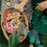 Eine Picknickszene zeigt den Freies Spiel: Fruits, winzige bemalte Holzfrüchte in einer Schale im Korb, umgeben von echten Äpfeln und einem gefalteten Tuch, passend zur nachhaltigen Ästhetik von KLICKKLACK.