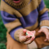 Ein Kind hält das Freies Spiel: Fruits, ein rundes Holzspielzeug, bemalt wie eine Wassermelone. Der natürliche Look spiegelt KLICKKLACKs Fokus auf nachhaltiges Design wider.