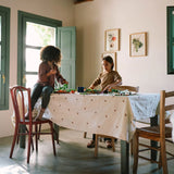 Kinder spielen mit Freies Spiel: Veggies auf einem Tisch mit Blumen-Tischdecke. Das Set umfasst frisches Gemüse und einen blauen Becher, ideal für kreatives, nachhaltiges Spielen in einem modernen, lichtdurchfluteten Raum.