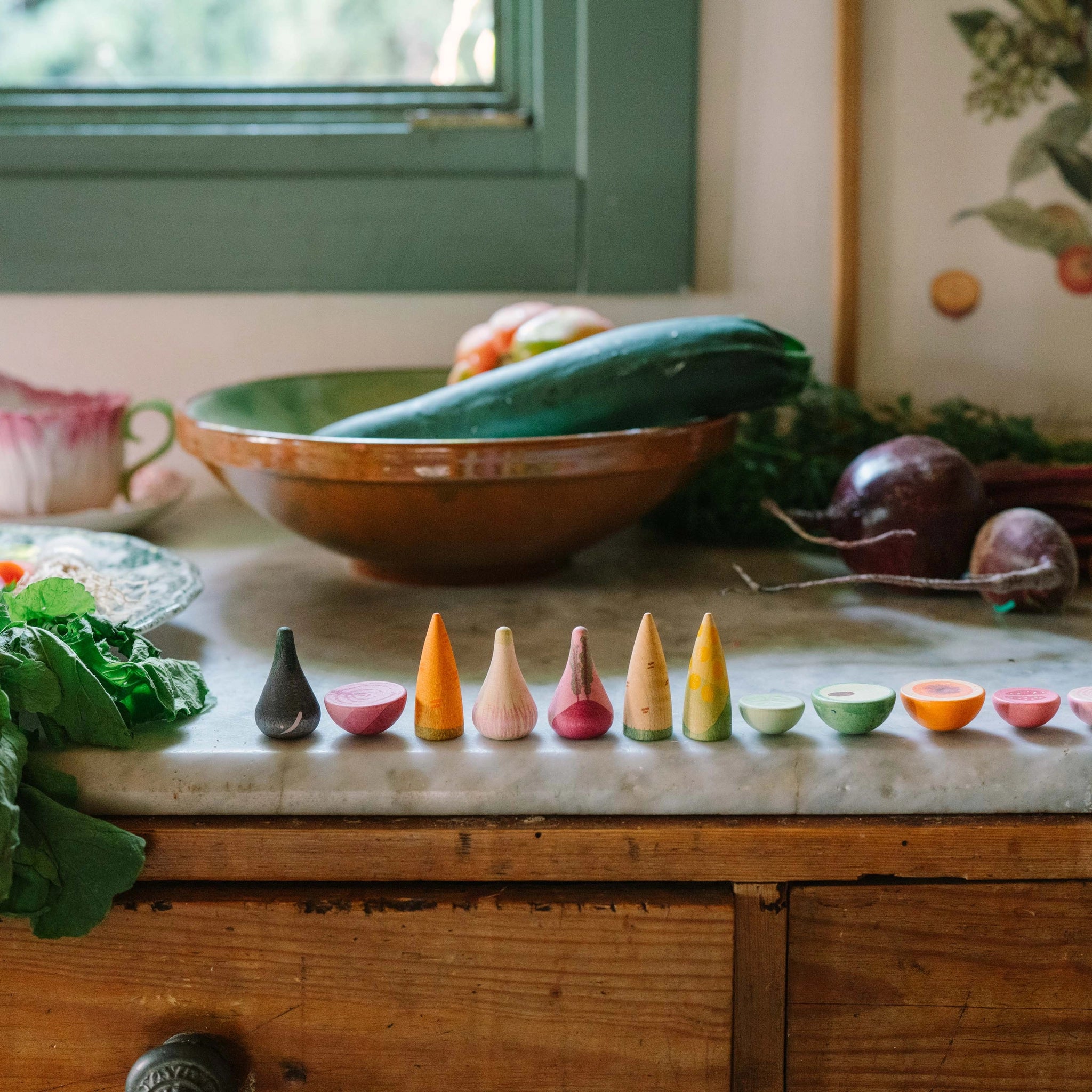 Freies Spiel: Veggies – Bunte, handgefertigte Holzgemüse auf einer rustikalen Küchentheke. Die detailreichen Miniaturen ergänzen das Arrangement aus frischem Gemüse und spiegeln kreatives, nachhaltiges Design wider.