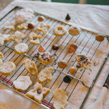 Frisch gebackene Zuckerplätzchen in Stern-, Blumen- und Kreisformen auf einem Gitter, verziert mit Sesam, Streuseln oder Schokoladenknöpfen, präsentiert als Teil von Freies Spiel: Bakes bei KLICKKLACK.