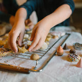 Kindliche, mehlbestäubte Hände arrangieren ungebackene Freies Spiel: Bakes Kekse mit Schokoladenknöpfen und Streuseln auf einem Rost. Ein kreativer Backmoment, der KLICKKLACKs nachhaltige, moderne Ästhetik verkörpert.