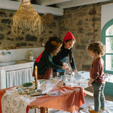 Drei Kinder backen fröhlich am rustikalen Tisch mit dem Set Freies Spiel: Bakes, das Schüsseln, Nudelholz und Ausstechformen umfasst, während sie Teig kneten. Ideal für kreative Backerlebnisse.