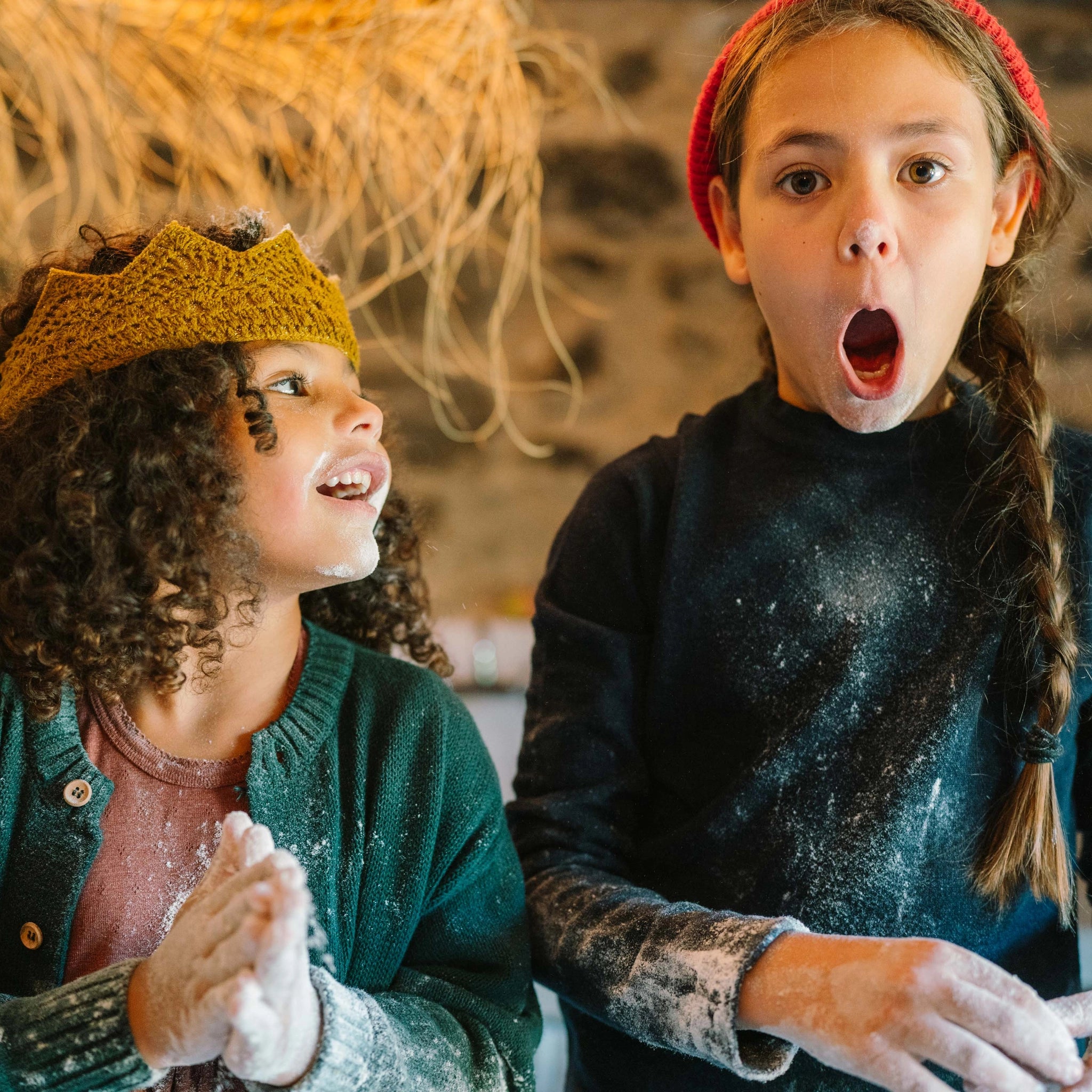 Zwei Kinder beim Backen: eines trägt eine gelbe Strickkrone, das andere eine rote Mütze, beide mit Mehl bedeckt, erleben Freies Spiel: Bakes in einer gemütlichen Küchenszene.