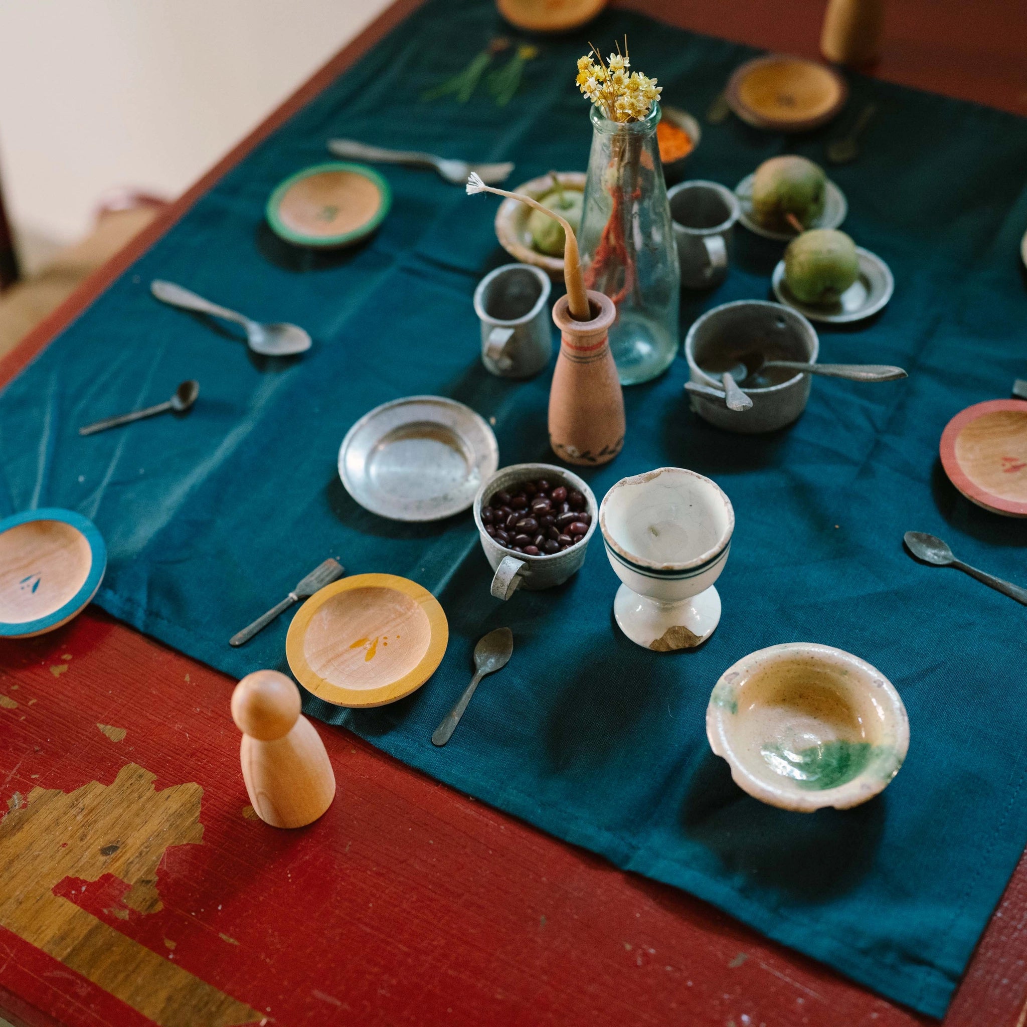 Freies Spiel: Dishes – Eine rustikale Anordnung von bemalten Holztellern, winzigen Löffeln, Metall- und Keramikgefäßen sowie natürlichen Akzenten auf einem Tisch, verkörpert nachhaltiges Design und zeitlose Ästhetik.