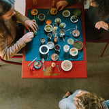 Kinder spielen mit dem Freies Spiel: Dishes-Set, sortieren Bohnen, Samen und Hülsenfrüchte in kleinen Schalen auf einem Tisch, umgeben von Holzfiguren und getrockneten Blumen.