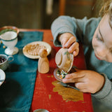 Ein Kind spielt konzentriert mit dem Freies Spiel: Dishes Set, bestehend aus einem kleinen Holzschälchen und weiteren Gefäßen, während es Bohnen sortiert. Perfekt für kreatives, nachhaltiges Spielen.