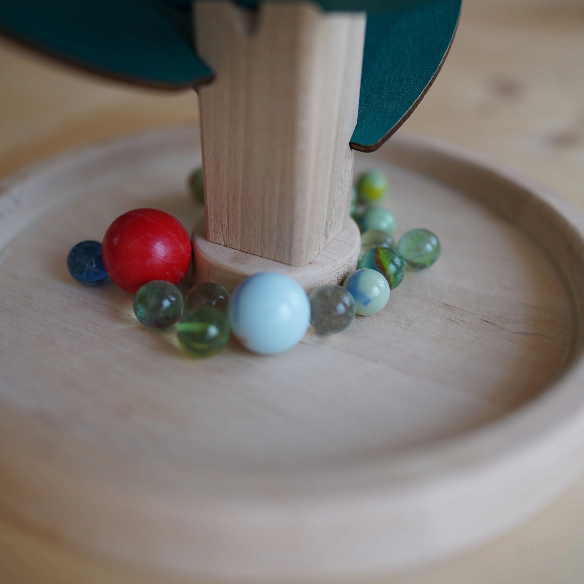 Klangbaum-Spielset: Ein runder Holzteller mit einem vertikalen Stamm und grünen Blättern aus Holz, umgeben von Murmeln, die beim Herabrollen harmonische Klänge erzeugen. Handgefertigt in Österreich.