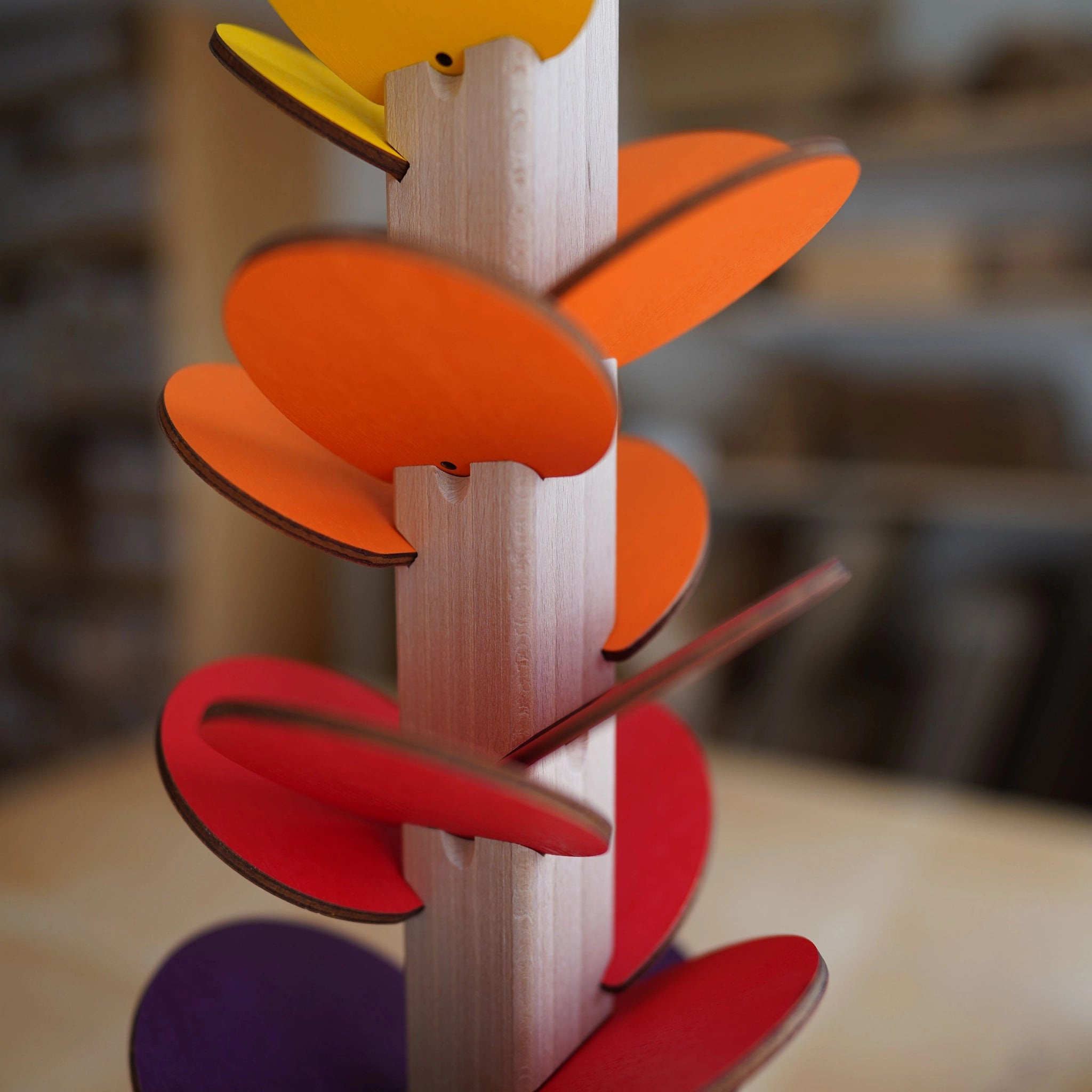 Klangbaum aus massivem Buchenholz mit farbigen, geschwungenen Birkensperrholzblättern, die harmonische Klänge erzeugen. Handgefertigt in Österreichs Familienbetrieb, vereint er nachhaltiges Design und ästhetische Freude.