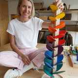 Eine Person hält den Klangbaum, ein spiralförmiges Murmelspiel aus massivem Buchenholz und farbigem Birkensperrholz, das in einem österreichischen Familienbetrieb gefertigt wurde, und lächelt dabei in die Kamera.