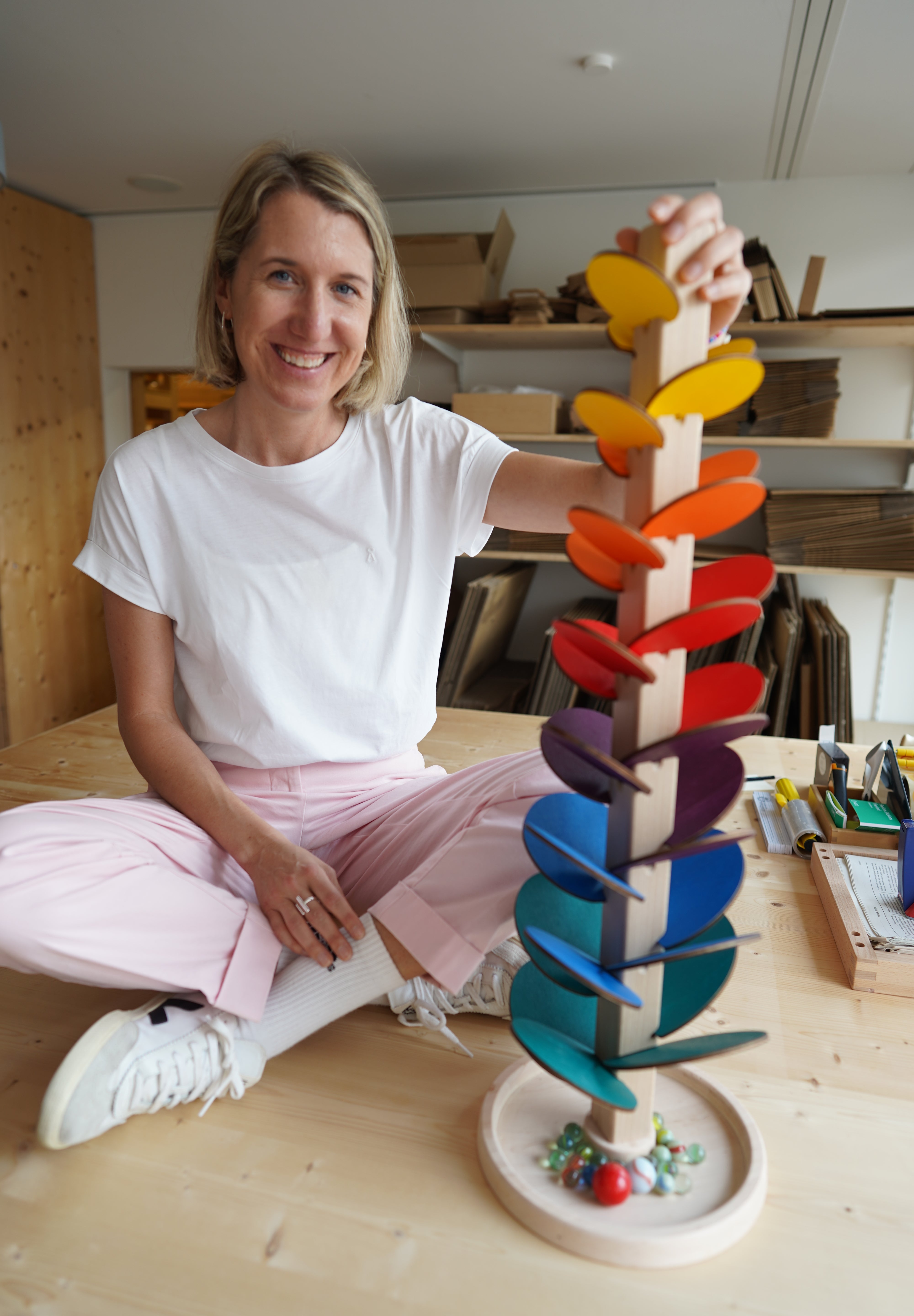 Eine Person hält den Klangbaum, ein spiralförmiges Murmelspiel aus massivem Buchenholz und farbigem Birkensperrholz, das in einem österreichischen Familienbetrieb gefertigt wurde, und lächelt dabei in die Kamera.