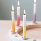 Steckfigur: Dip-Dye Regenbogen Festtags-Kerzen auf einem schlichten, runden Holzkerzenhalter. Die Kerzen sind in sanften Farbverläufen getaucht und brennen, ideal für festliche Tischdekorationen.