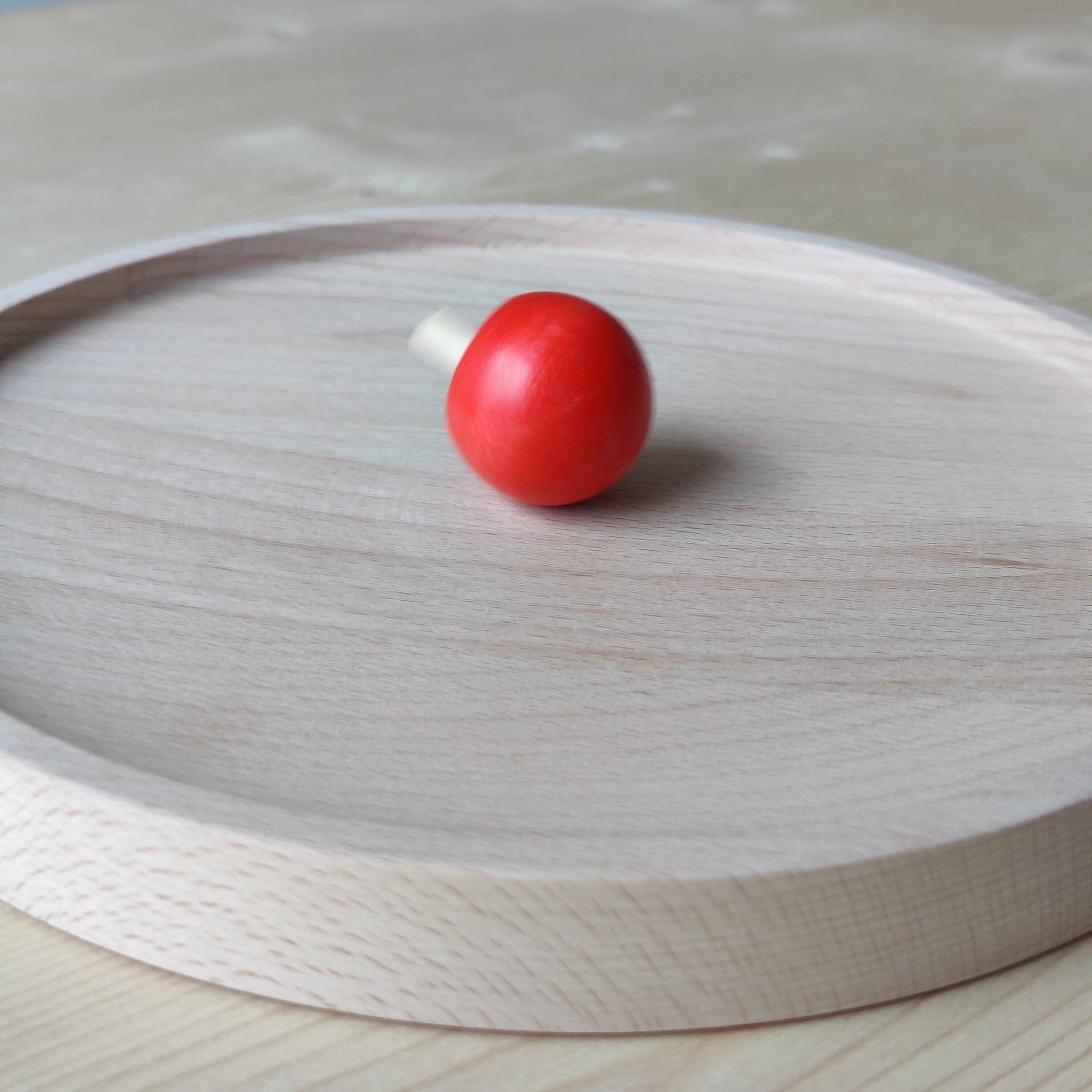 Kreiselteller aus massivem Buchenholz mit erhöhtem Rand, der ein Wegrollen verhindert, präsentiert auf einem Tisch. Perfekt zum Spielen mit Holzkreiseln, handgefertigt in Deutschland für nachhaltigen Spaß.