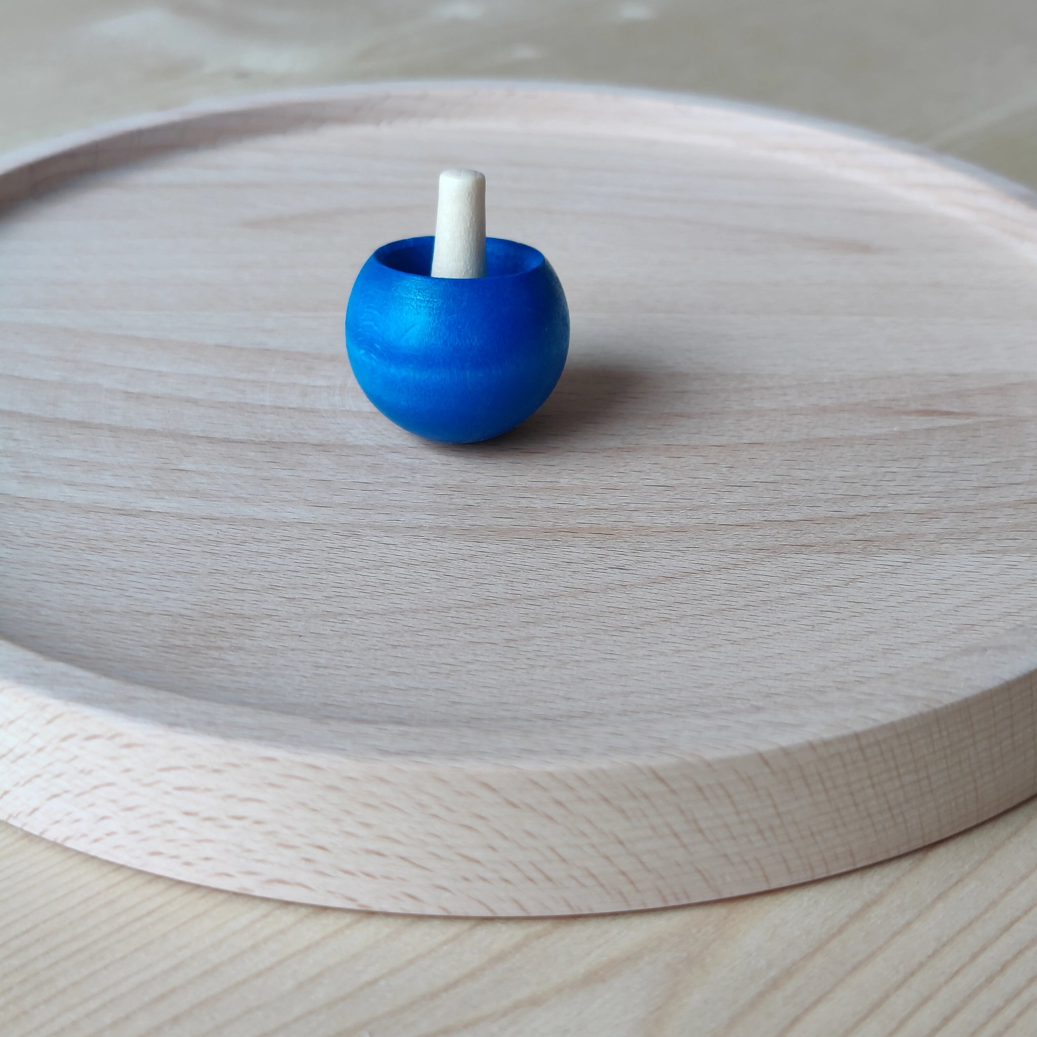 Kreiselteller aus massivem Buchenholz, auf einem Tisch platziert. Der erhöhte Rand verhindert das Wegrollen von Spielzeugkreiseln. Handgefertigt in Deutschland, vereint es Ästhetik und Nachhaltigkeit für moderne Nutzer.