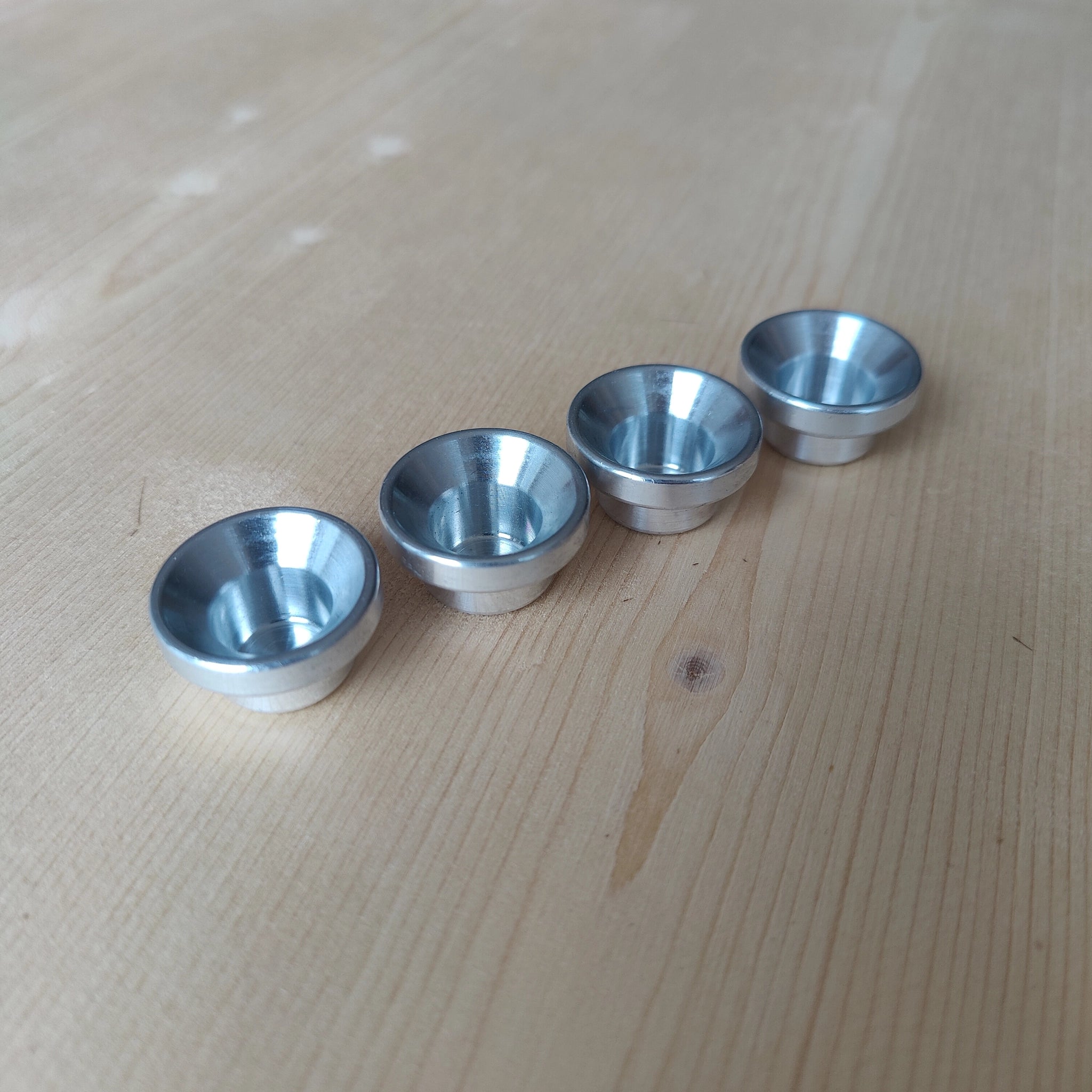 Steckfigur: Kerzenhalter Aluminium, vier identische, kleine, flache Schalen aus silbernem Aluminium mit konischer Innenseite und zylindrischem Sockel, auf heller Holzoberfläche, ideal für Grimm's-Kerzen auf Festtagsring oder -spirale.