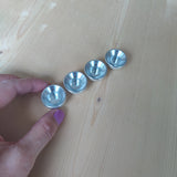 Vier kleine, glänzende Steckfigur: Kerzenhalter Aluminium aus hochwertigem Aluminium, perfekt für Grimm's-Kerzen, präsentiert auf einem hellen Holztisch. Eine Hand hält den linken Kerzenhalter, ideal für Festtagsdekorationen.