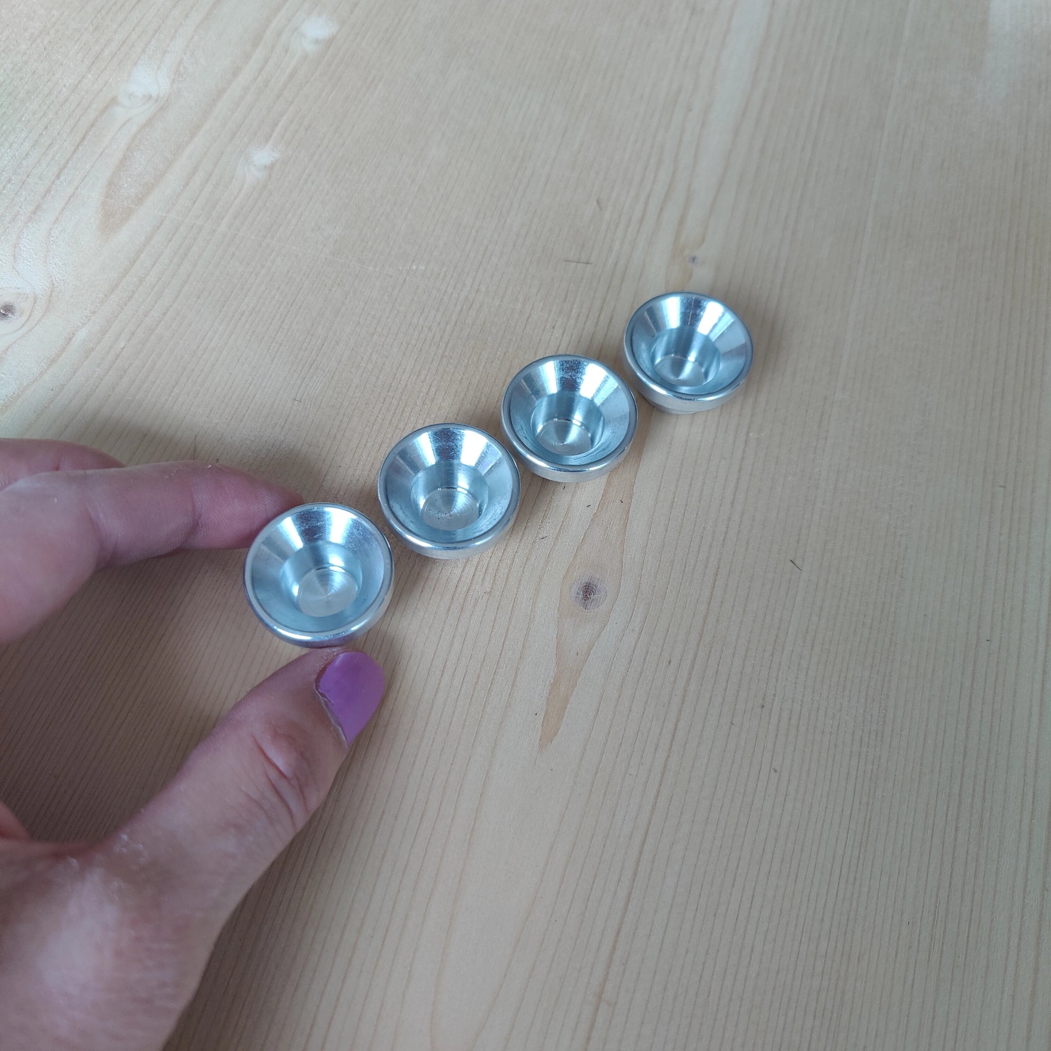 Vier kleine, glänzende Steckfigur: Kerzenhalter Aluminium aus hochwertigem Aluminium, perfekt für Grimm's-Kerzen, präsentiert auf einem hellen Holztisch. Eine Hand hält den linken Kerzenhalter, ideal für Festtagsdekorationen.
