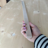 Hand hält Großer Schuhlöffel aus glattem Buchenholz, ausgestattet mit einem praktischen Lederband zum Aufhängen. Ideal für bequemes Anziehen, handgefertigt in der Schweiz und beliebt als Geschenk.