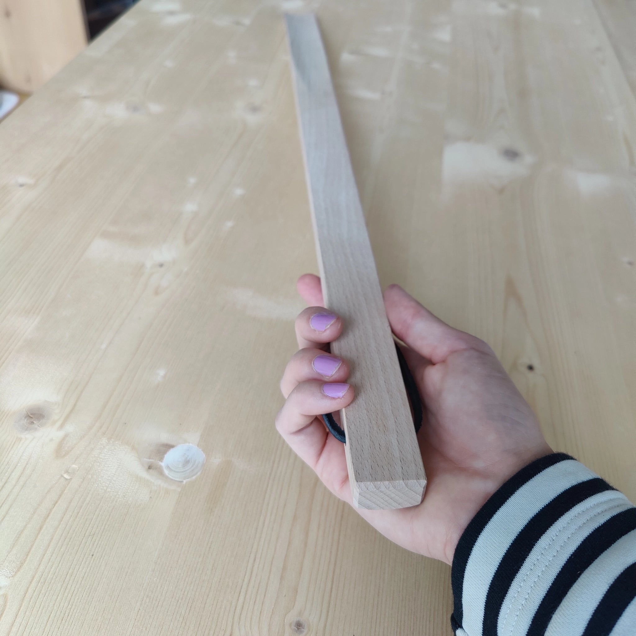 Hand hält Großer Schuhlöffel aus glattem Buchenholz, ausgestattet mit einem praktischen Lederband zum Aufhängen. Ideal für bequemes Anziehen, handgefertigt in der Schweiz und beliebt als Geschenk.