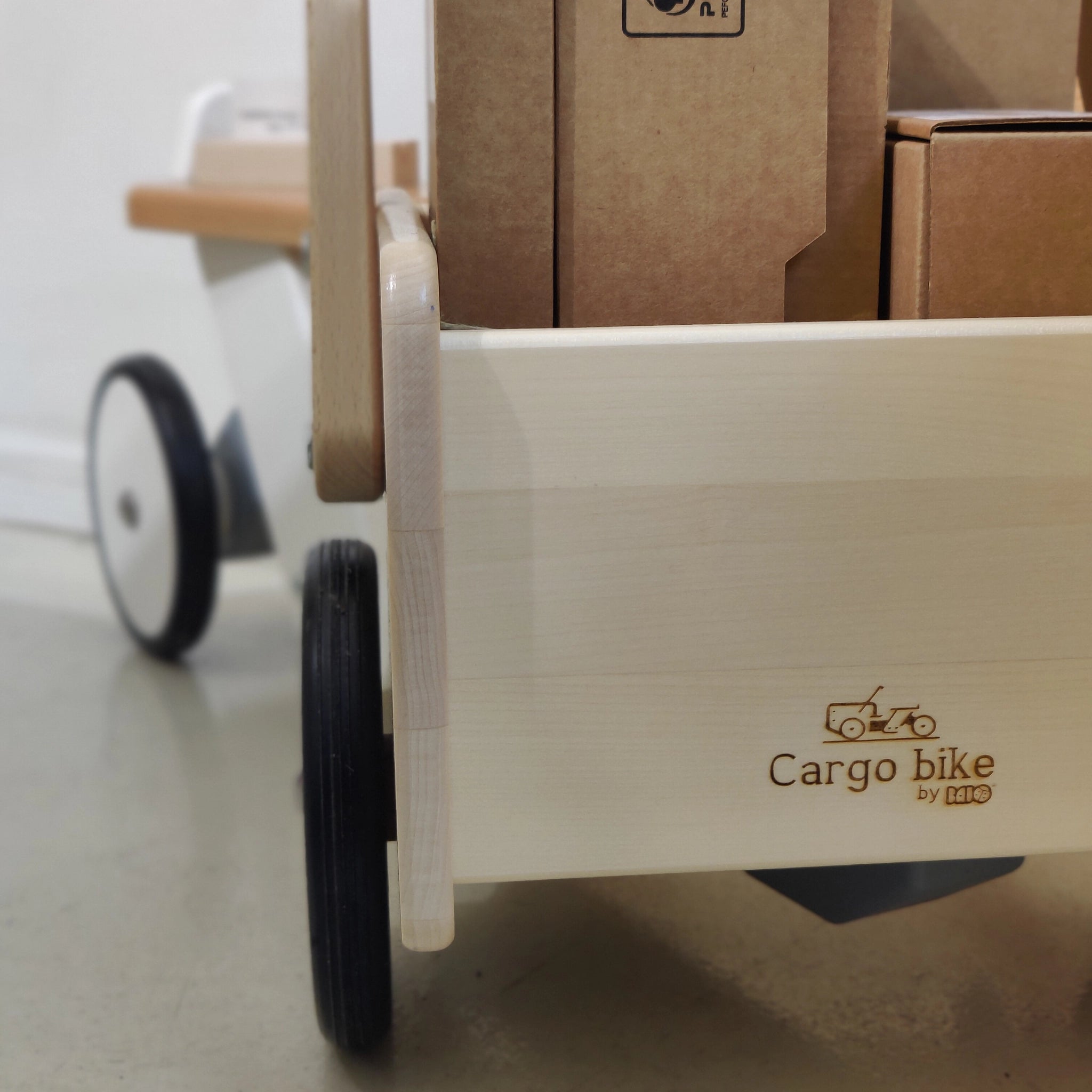 Holzfahrzeug: Lastenrad aus Buchen- und Ahornholz mit einer stabilen, kippsicheren Konstruktion. Nahaufnahme zeigt den Holz-Logo-Brand Cargo bike und beladene Pappkartons im Vorderradkorb.