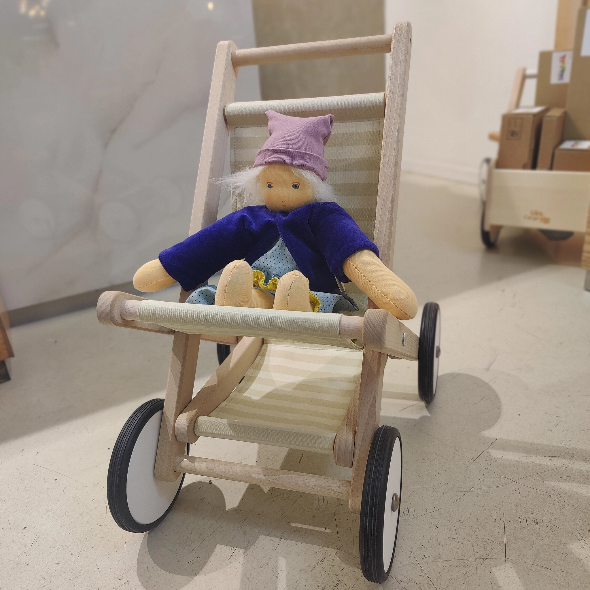 Puppenbuggy natur aus robustem Holz, mit Leinensitz und vier Rädern, enthält weiche Stoffpuppe im lila Jäckchen. Handgefertigt in Polen, ideal für Puppen und Kuscheltiere.