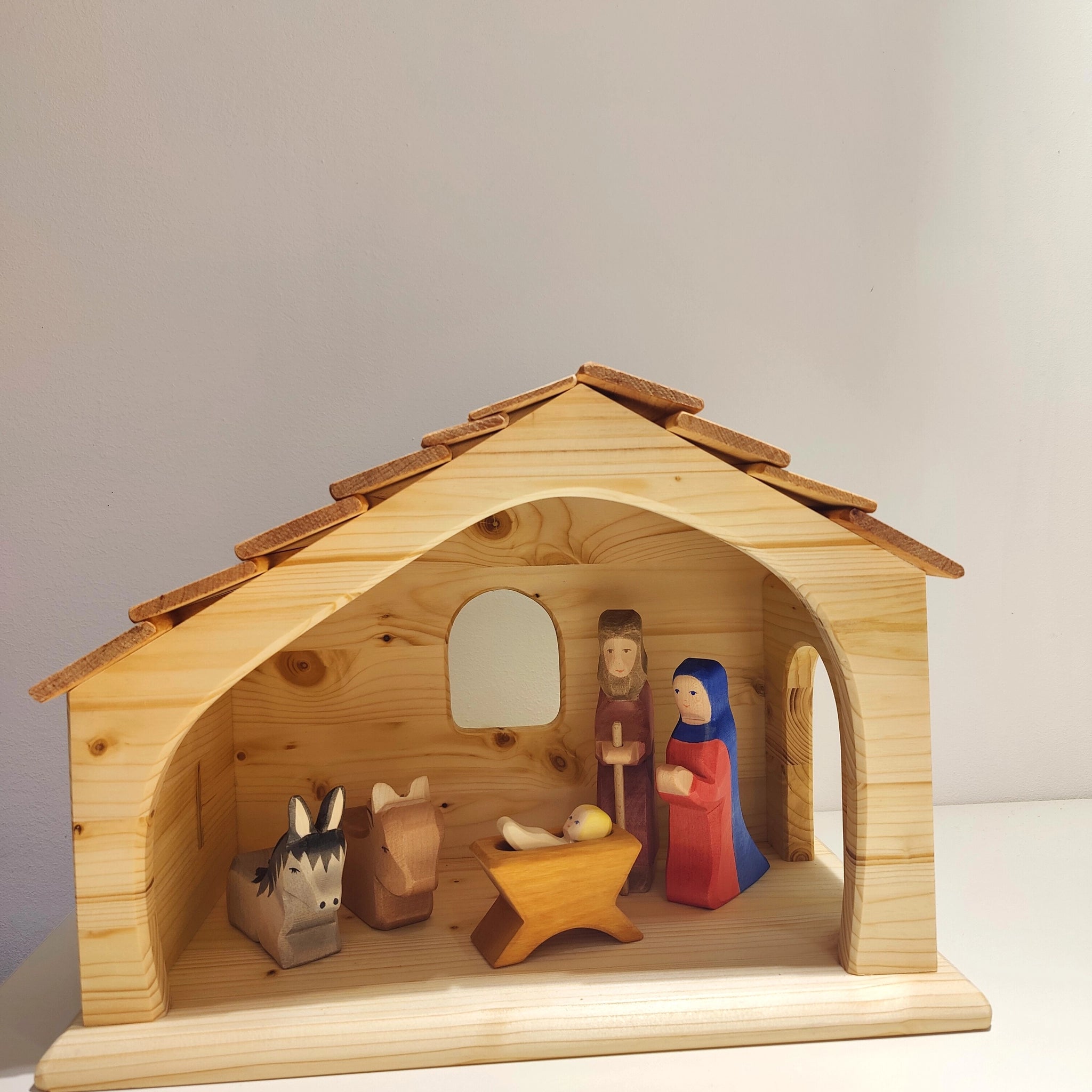 Krippe aus massivem Fichtenholz mit handgeschnitzten Figuren von Josef, Maria und dem Jesuskind in einem schlichten Stall mit Schindeldach und Fenster, gefertigt in einer deutschen Holzmanufaktur.