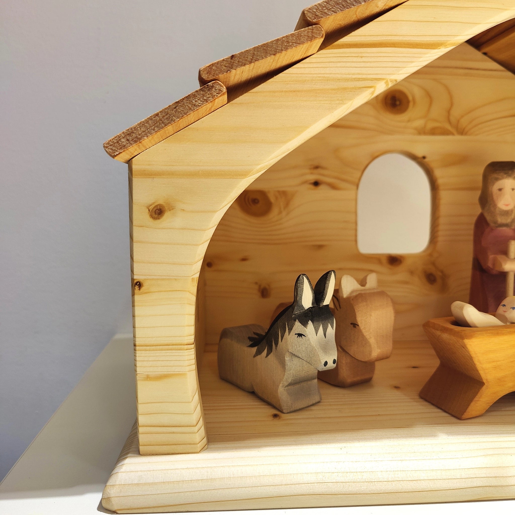 Krippe aus massivem Fichtenholz mit robustem Schindeldach, zeigt geschnitzte Tiere, ein Baby in der Krippe und eine stehende Figur, ideal als stilvoller, nachhaltiger Weihnachtsstall von KLICKKLACK.