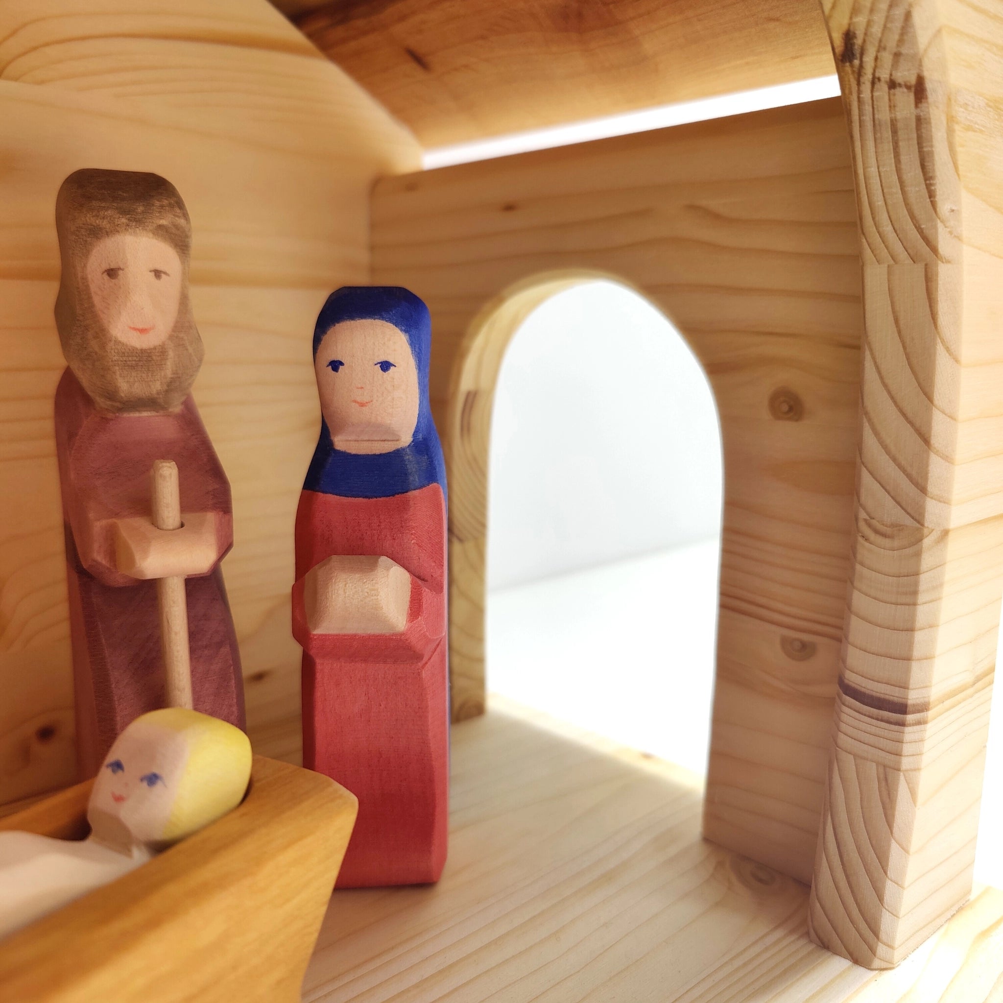 Krippe aus massivem Fichtenholz mit handbemalten Figurinen von Josef, Maria und dem Jesuskind, in einem robusten, einfach gestalteten Stall mit Schindeldach, ideal für nachhaltige und ästhetische Dekoration.