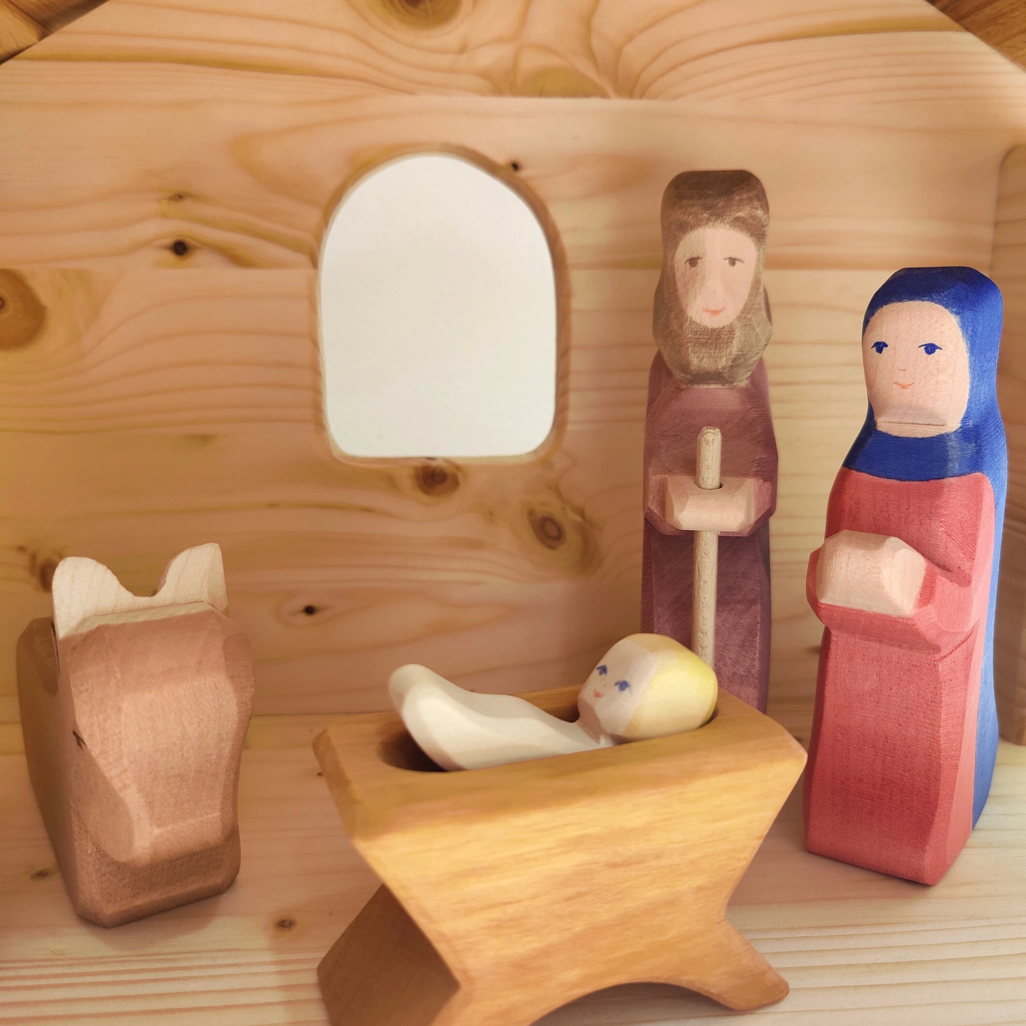 Krippe aus handgeschnitztem Fichtenholz mit Leinöl veredelt, zeigt Baby Jesus, Joseph mit Stab, Maria in Rot-Blau und Tierkopf im Stall mit robustem Schindeldach, gefertigt in deutscher Holzmanufaktur.