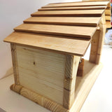 Handgefertigte Krippe aus massivem Fichtenholz mit robustem Schindeldach, dekorativer Seitentür und rückseitigem Fenster, auf einer weißen Fläche platziert. Ideal als Krippe oder Stall, hergestellt in Deutschland.