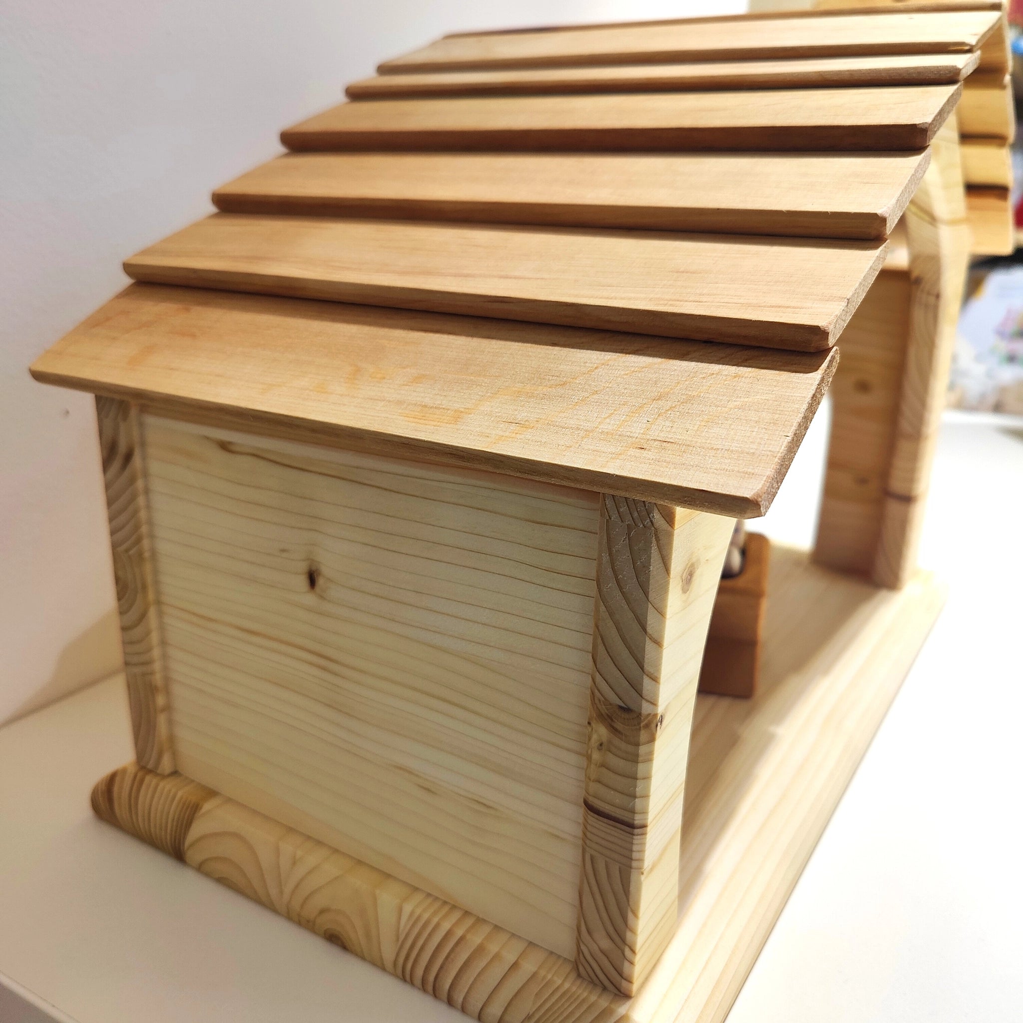 Handgefertigte Krippe aus massivem Fichtenholz mit robustem Schindeldach, dekorativer Seitentür und rückseitigem Fenster, auf einer weißen Fläche platziert. Ideal als Krippe oder Stall, hergestellt in Deutschland.