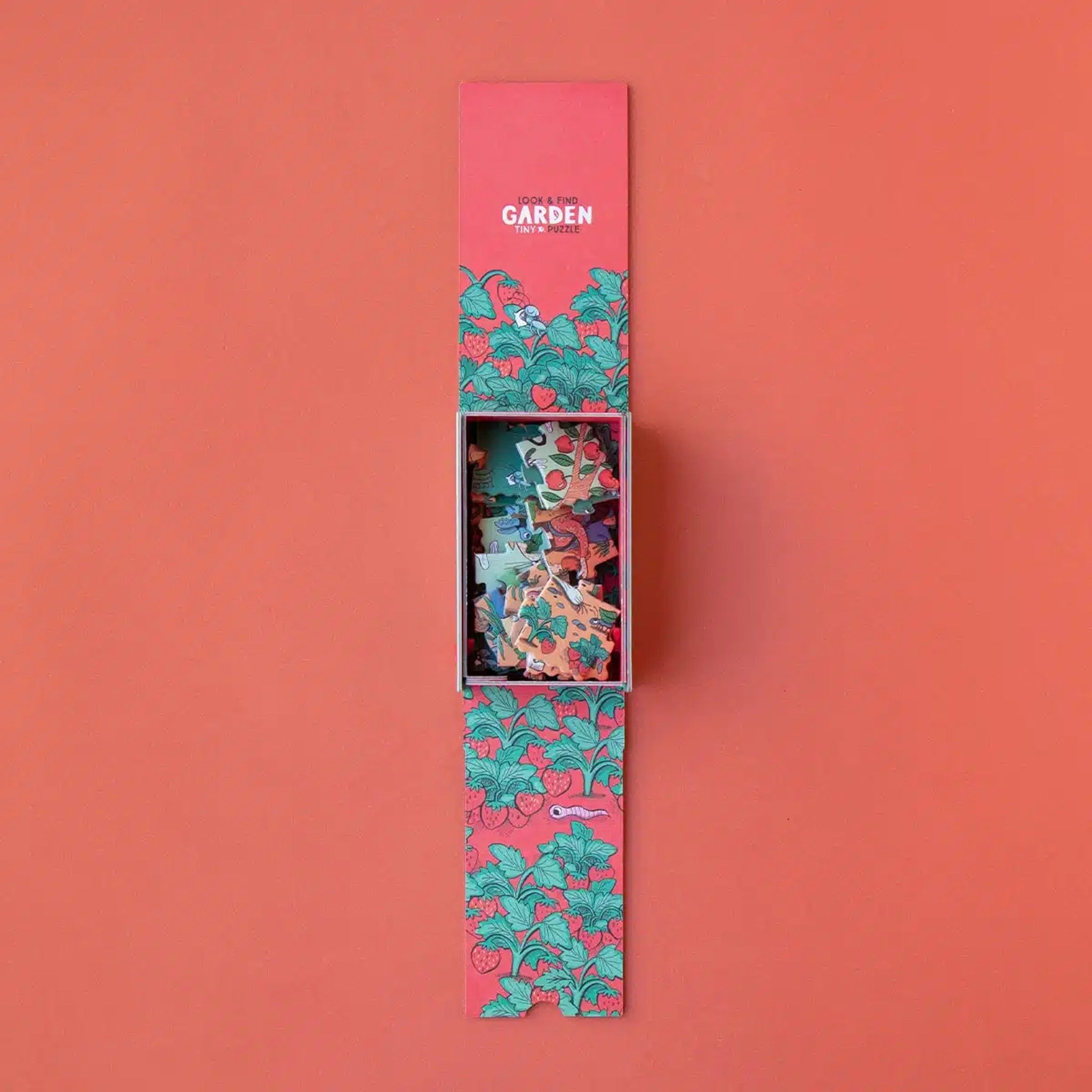 Minipuzzle: Garden – Schmale Schiebeschachtel mit stilisiertem Erdbeer-Ranken-Design, zeigt lose Puzzleteile mit Garten- und Beerenmotiven. Nachhaltig aus FSC-Papier, 24 Teile, ideal für Kinder ab 4 Jahren.