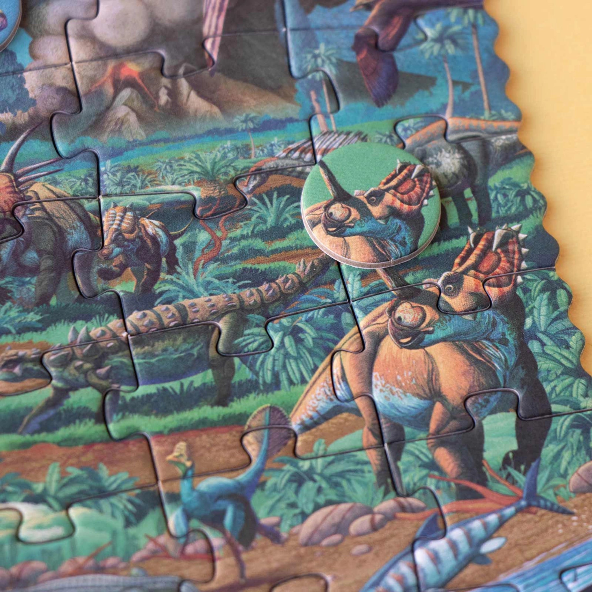 Minipuzzle: Dinosaurs zeigt ein teils fertiges 50-teiliges Puzzle mit Dinosauriern, darunter hornige Ceratopsier und ein Ankylosaurier, plus Vulkan. Perfekt für Kinder, aus nachhaltigen Materialien, hergestellt in Spanien.