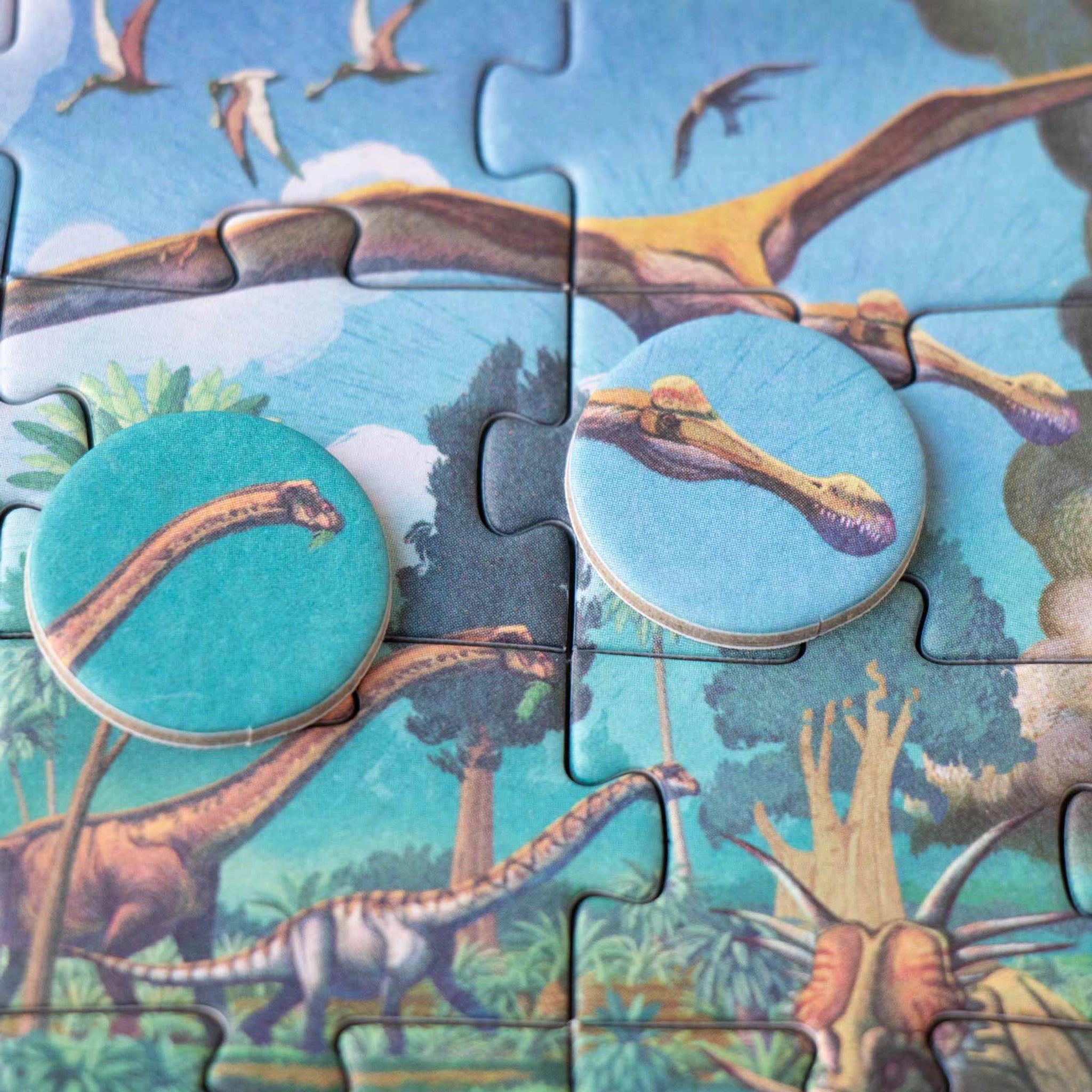 Minipuzzle: Dinosaurs, ein 50-teiliges Dinosaurier-Puzzle mit Sauropoden und Pterosauriern, zwei runde Kartonmarken zeigen Dinosaurierköpfe, aus FSC-Papier und recyceltem Karton, ideal für Kinder ab 5 Jahren.