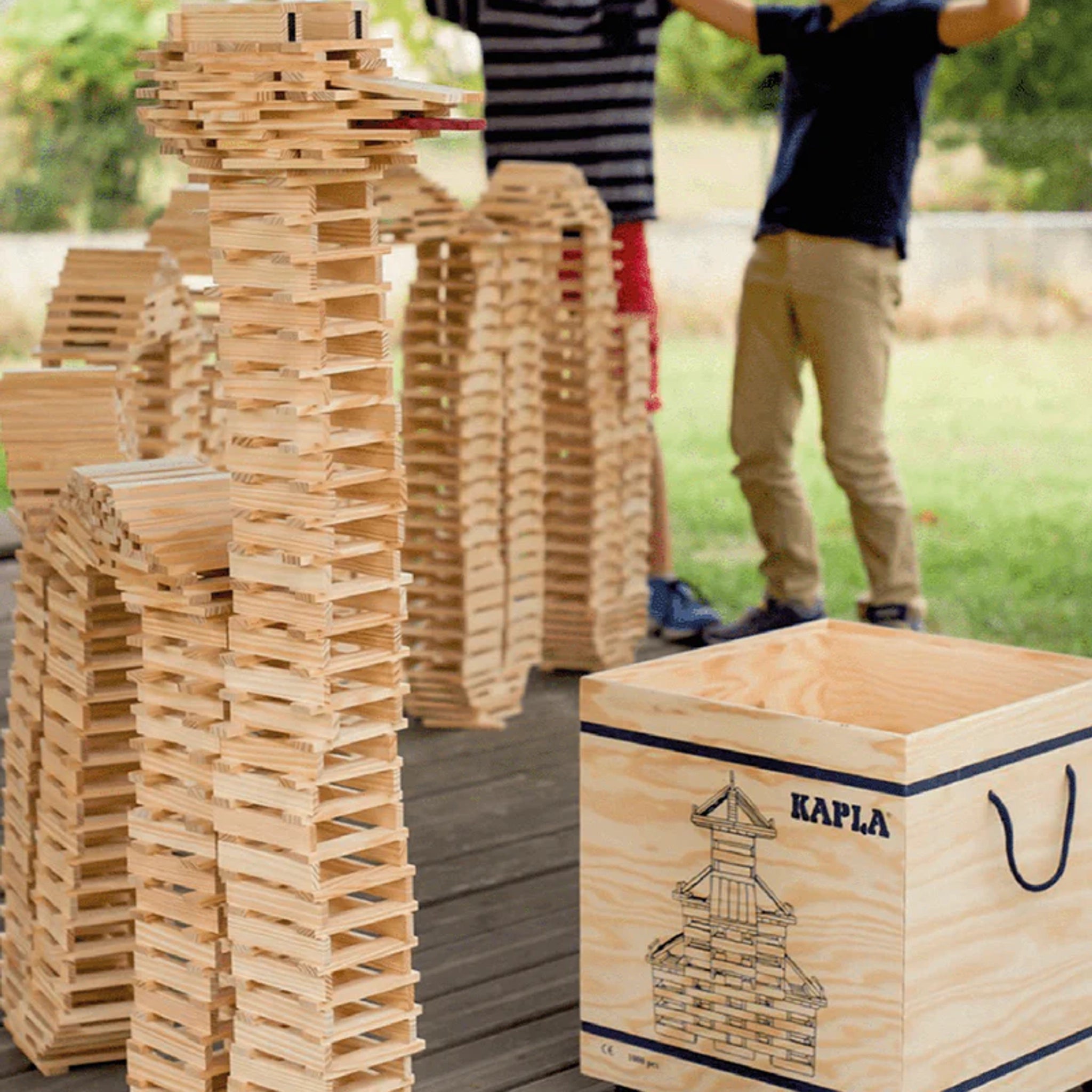 Bausteine: 500er Kiste, bestehend aus gleichmäßigen Holzplättchen, die Kinder zu Türmen stapeln. Im Vordergrund die stabile Holzkiste mit KAPLA-Aufschrift, inklusive Anleitungsheft, nachhaltig produziert in Frankreich.