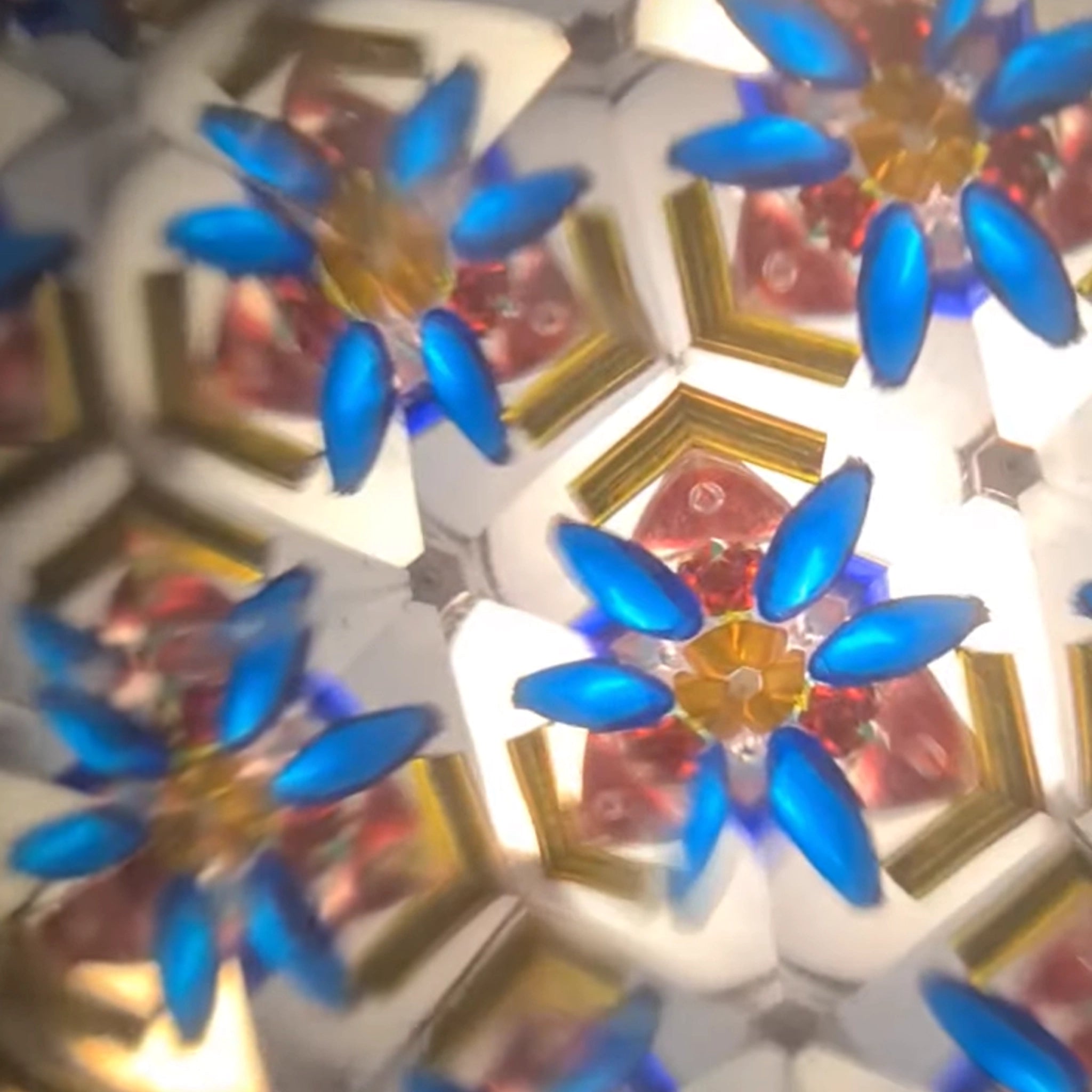Kaleidoskop türkisblau: Innenansicht eines kaleidoskopischen Musters mit blauen Blütenblättern und gold-roten Formen, handbemalt auf massivem Eschenholz, hergestellt in Österreich, geeignet für Kinder ab 3 Jahren.