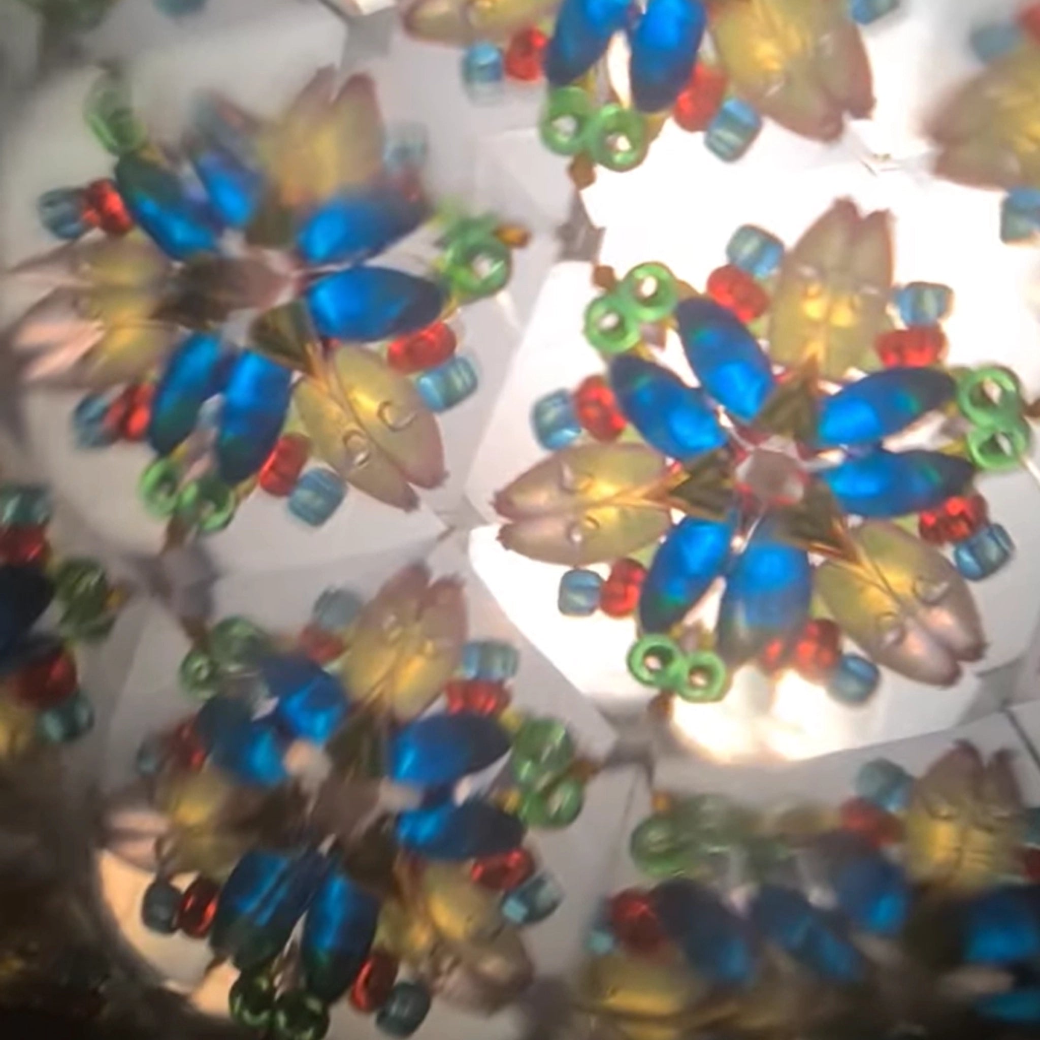 Kaleidoskop türkisblau: Innenansicht zeigt symmetrische, blumenartige Muster aus bunten Perlen, die faszinierende, geometrische Formen bilden. Handgefertigt aus Eschenholz, ideal für Kinder ab 3 Jahren.