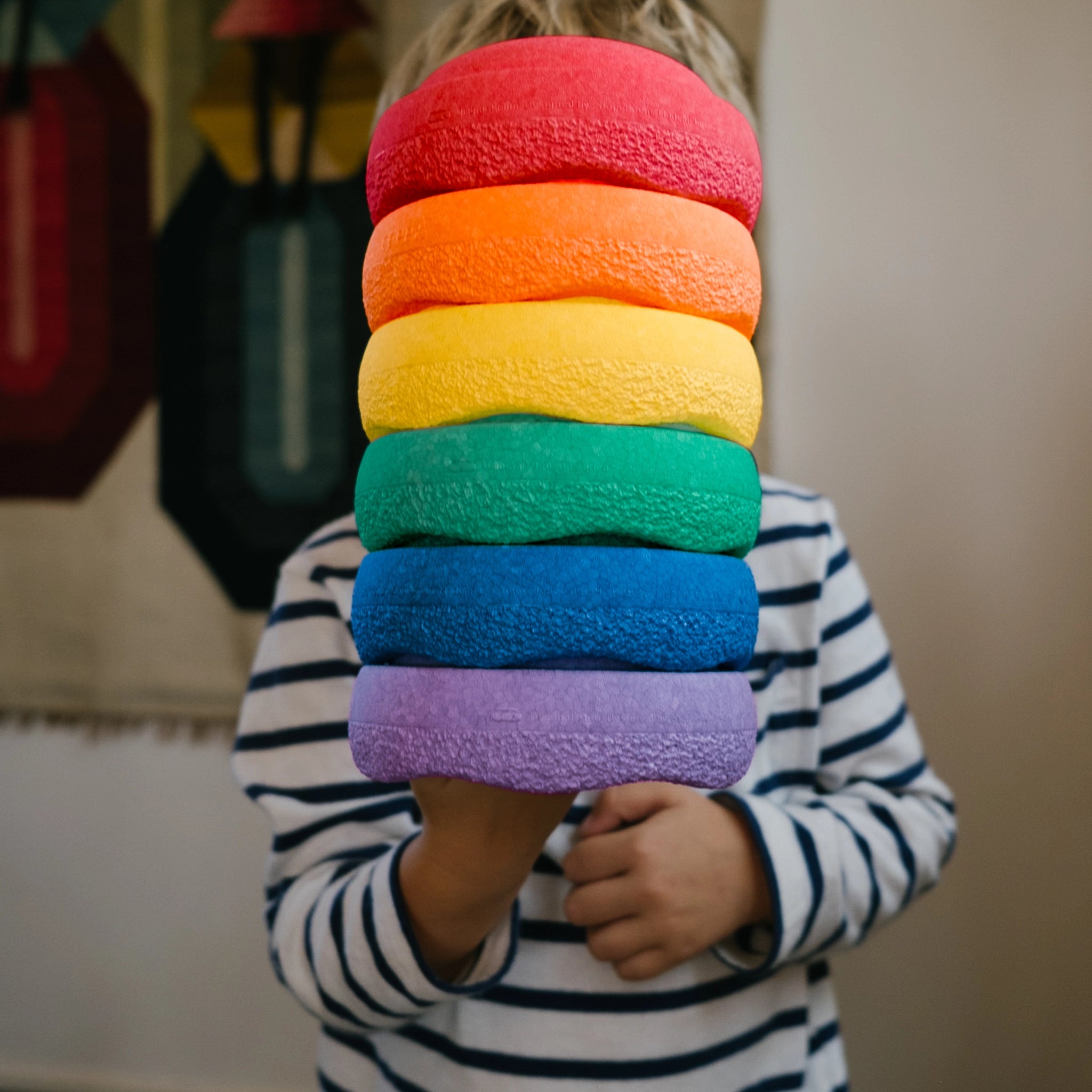 Ein Kind hält die Stapelstein: Mini Regenbogen Classic (6 Steine), eine hohe, strukturierte Schaumstoffring-Stapel in Regenbogenfarben. Perfekt für nachhaltiges, kreatives Spiel, passend zur modernen Ästhetik von KLICKKLACK.